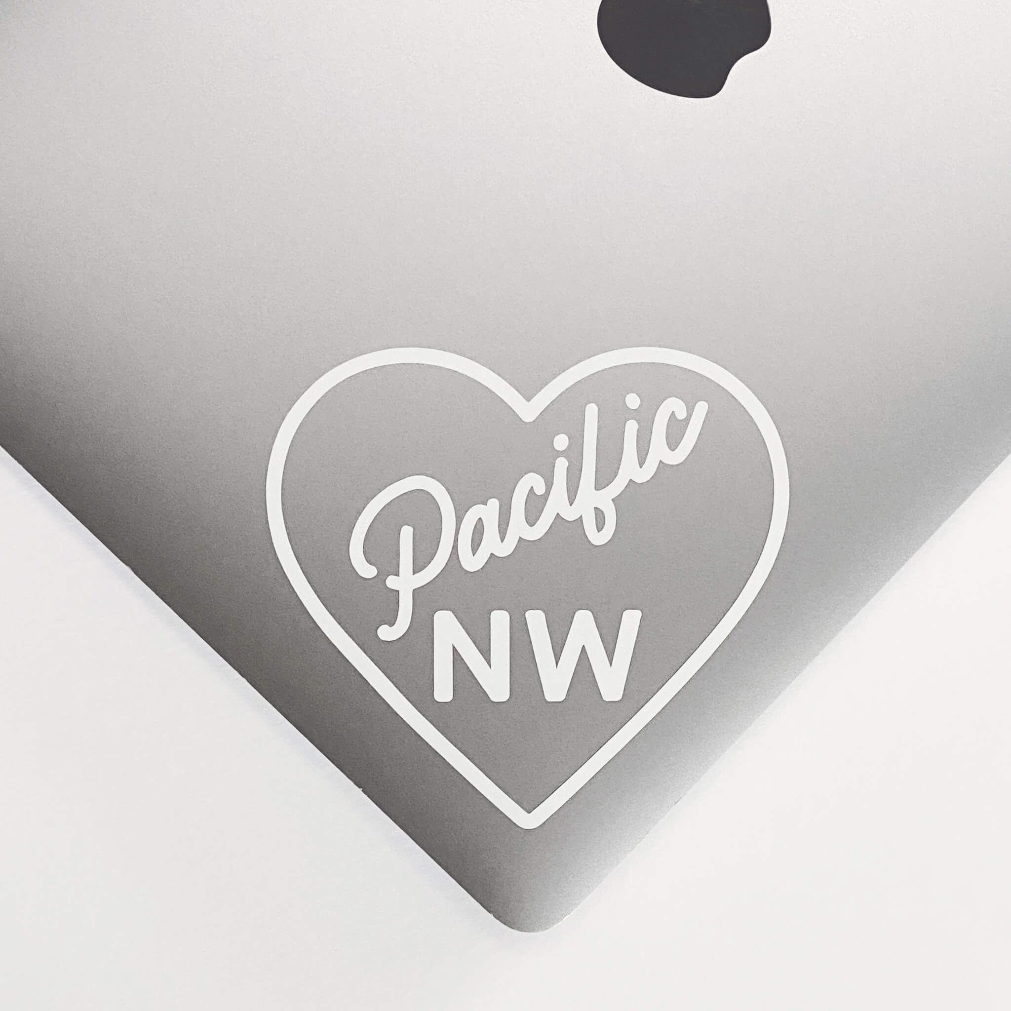 white 'pacific nw" and heart sticker on laptop